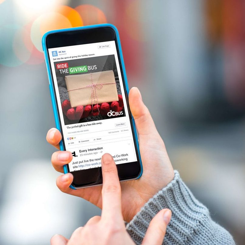 Woman holding phone looking at OC Bus social media add